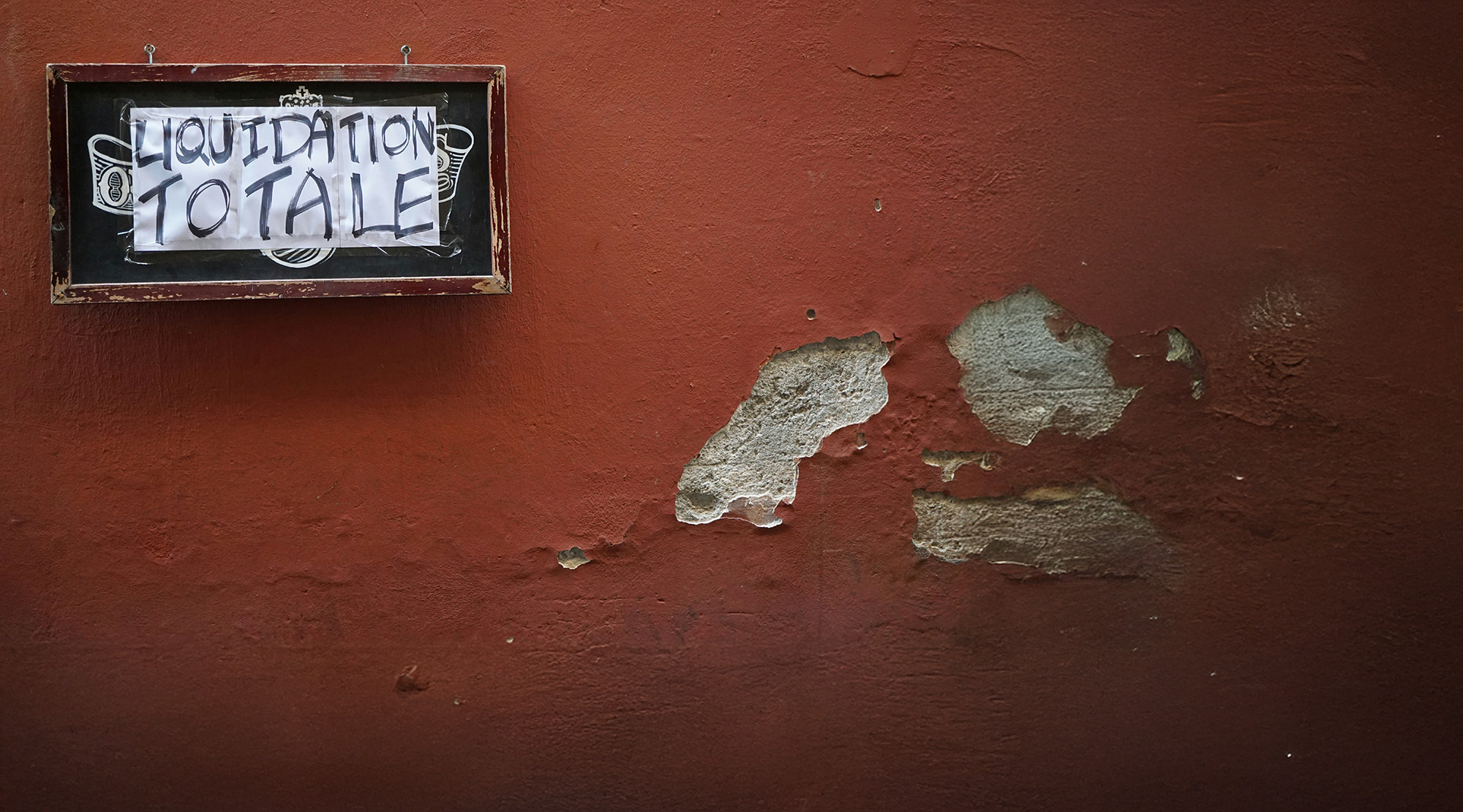 Ein Schild hängt an einer roten Wand mit der Aufschrift "Liquidation totale". Es soll eine Sanierungsberatung symbolisieren